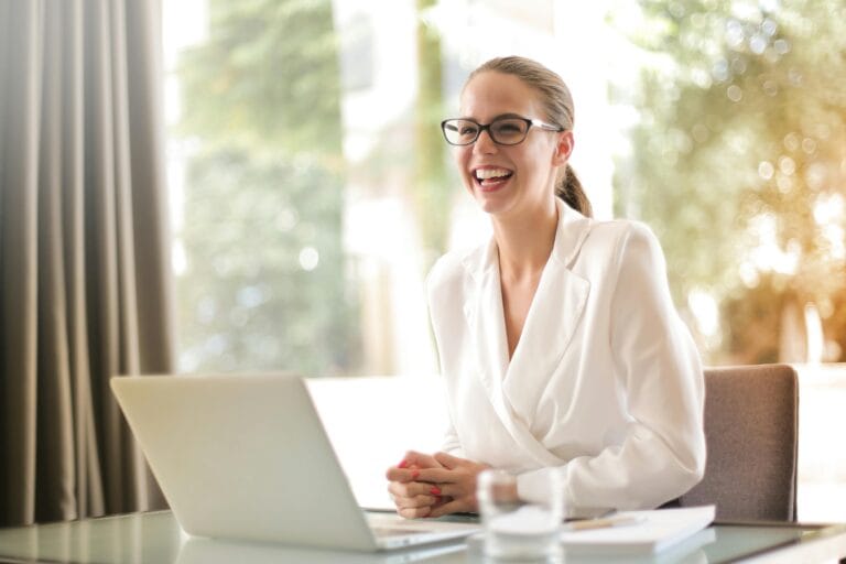 Alternative Careers for Remote Workers Who Just Got Laid Off Cheerful businesswoman in glasses working on a laptop, in a bright and modern office setting.