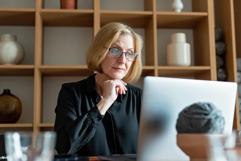 Senior businesswoman with glasses concentrating on work at a home office with a laptop.