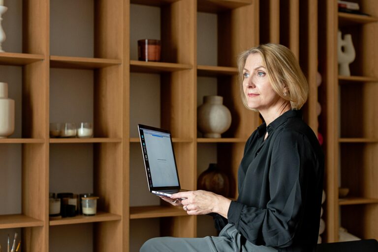A focused middle-aged woman working on her laptop in a stylish home office setting.