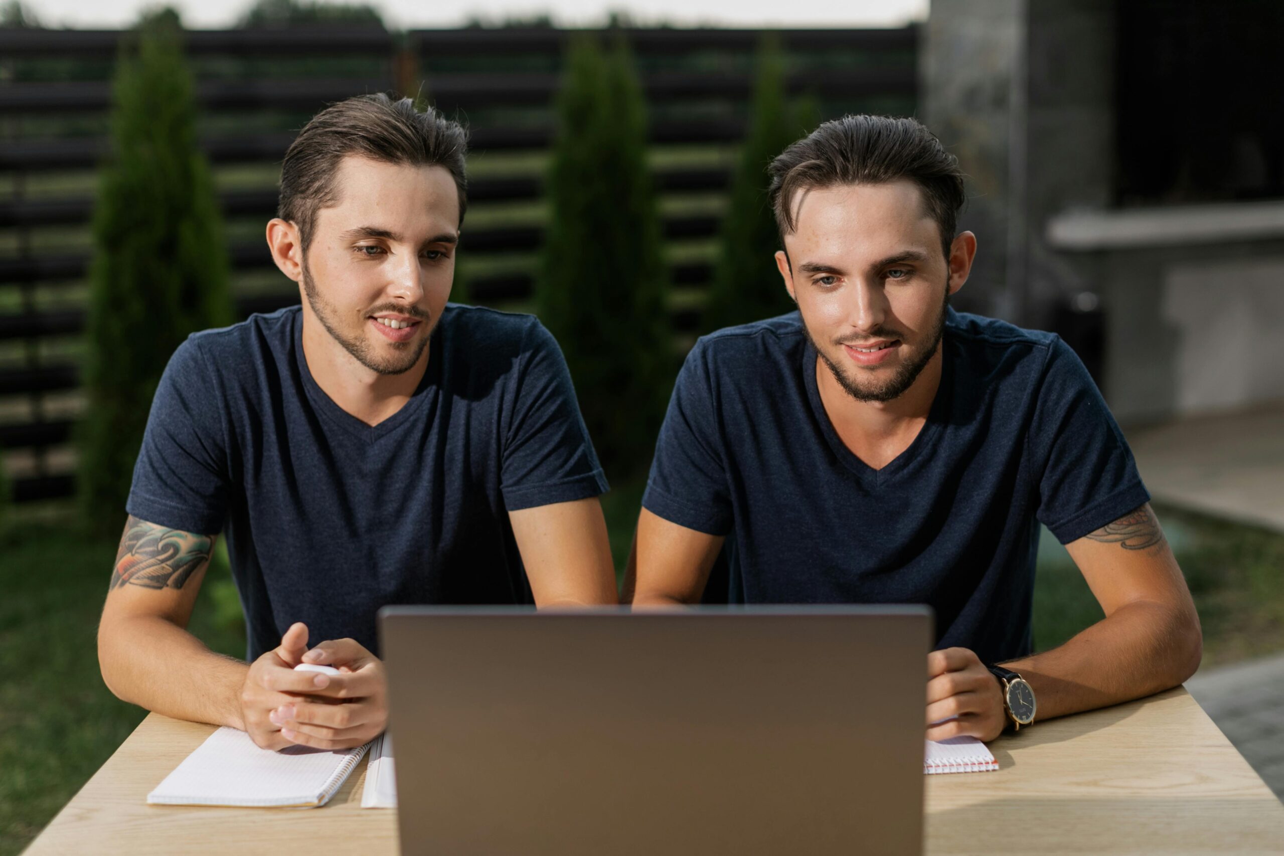 Two twin brothers focused on a laptop, collaborating outside on a warm day.