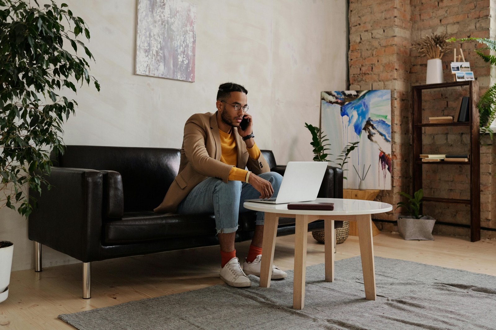 Adult man multitasking on phone and laptop in a cozy home office setting.