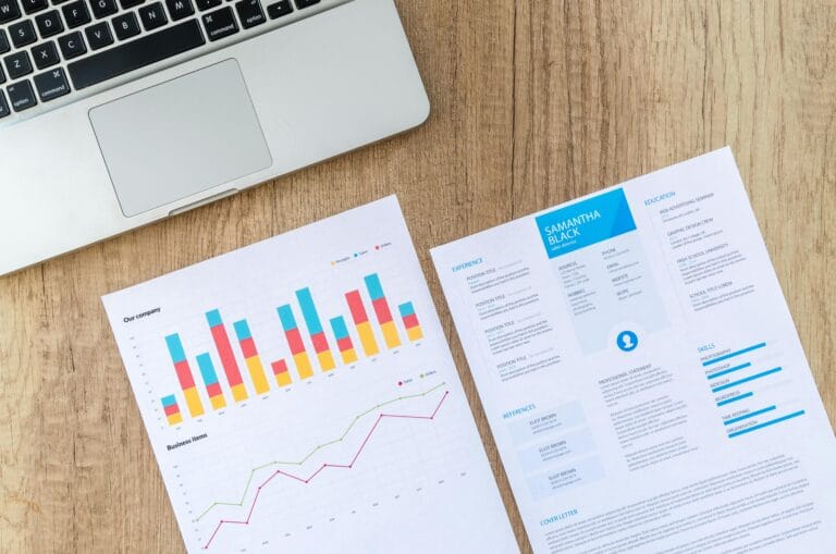 How to Make Your Remote Resume ATS-Proof (and Actually Get Seen) Top view of a laptop, charts, and resume on a wooden desk, showcasing business analysis and job application.