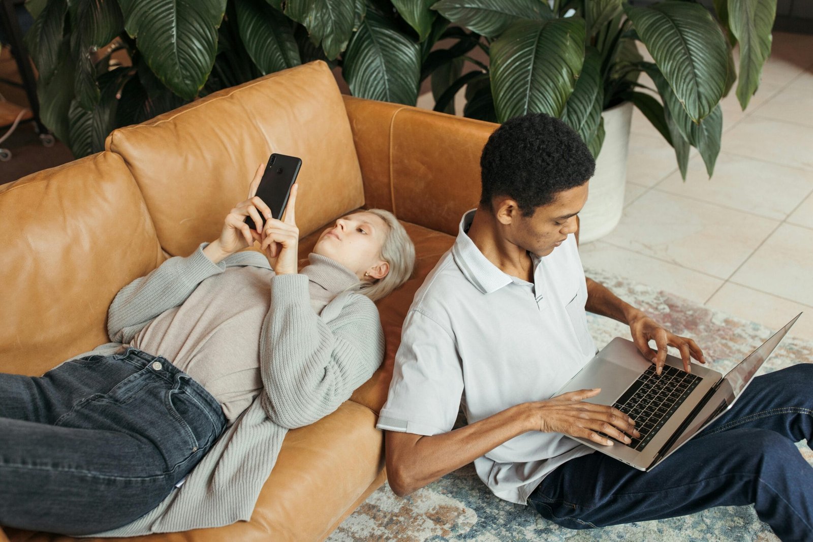 Two diverse co-workers relaxing and working on a sofa with a laptop and smartphone.