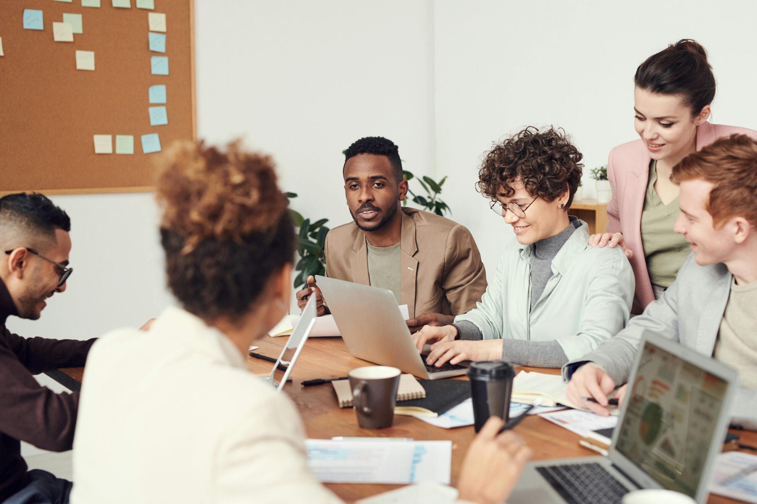 Contractor vs. Employee in Remote Roles: What’s Right for You? Multicultural team engaged in a collaborative office meeting, discussing ideas around a table with laptops.